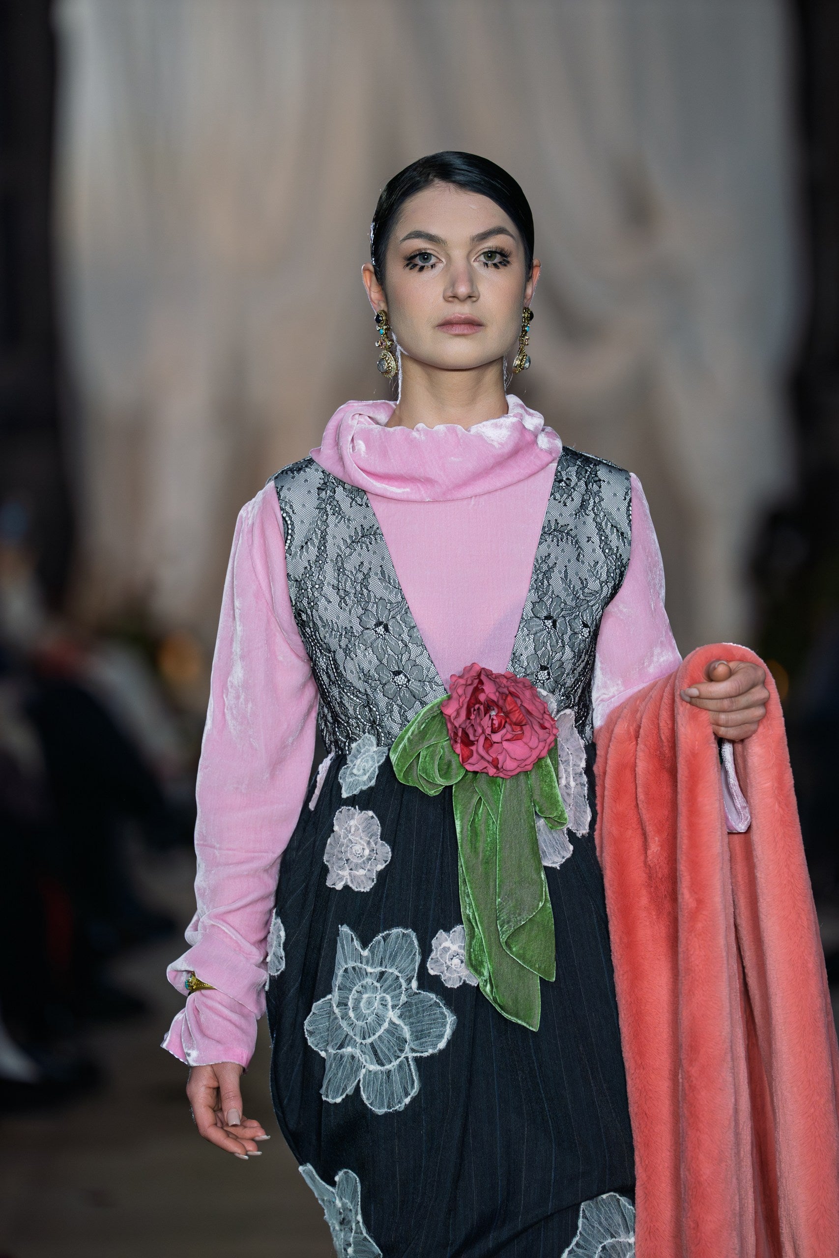 Model wearing a pink blouse with a black floral dress on a runway