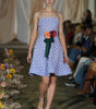 Model wearing a light purple dress with floral accessories on a runway.