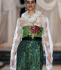 Model wearing a green and white dress with floral details on a runway.