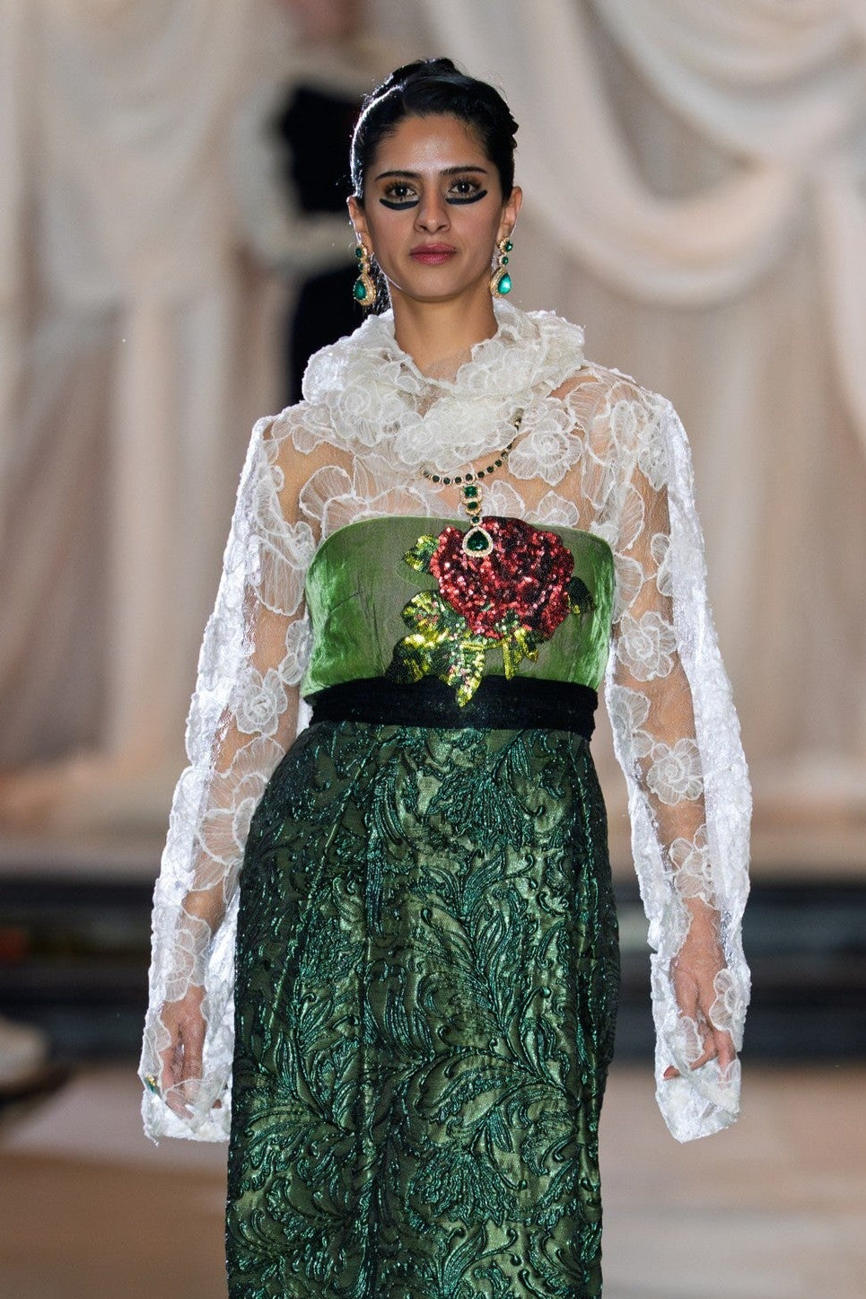 Model wearing a green and white dress with floral details on a runway.