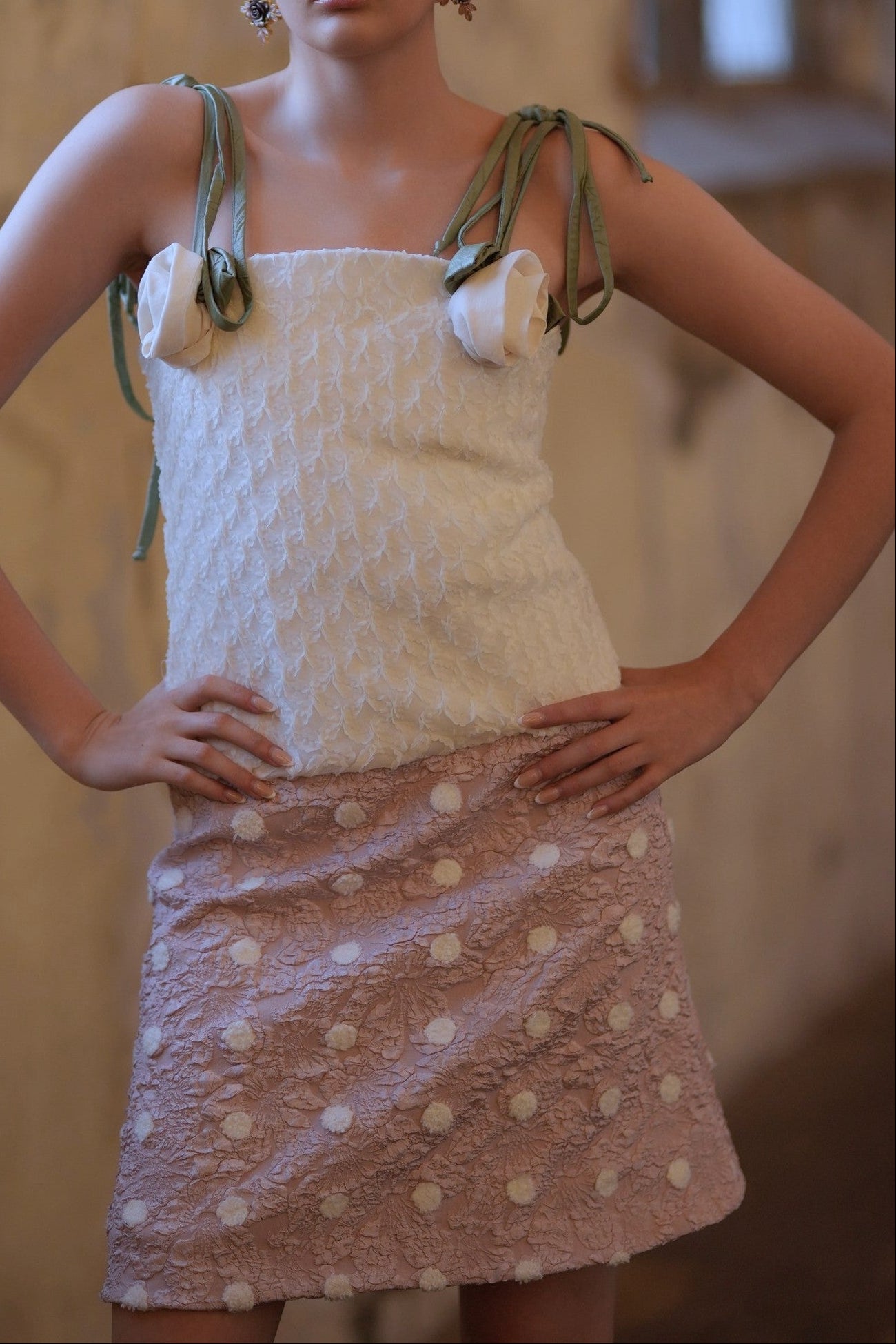 Model wearing a white textured top and polka dot skirt in an indoor setting