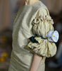 Model wearing a beige dress with a large ruffled pocket holding a white object.