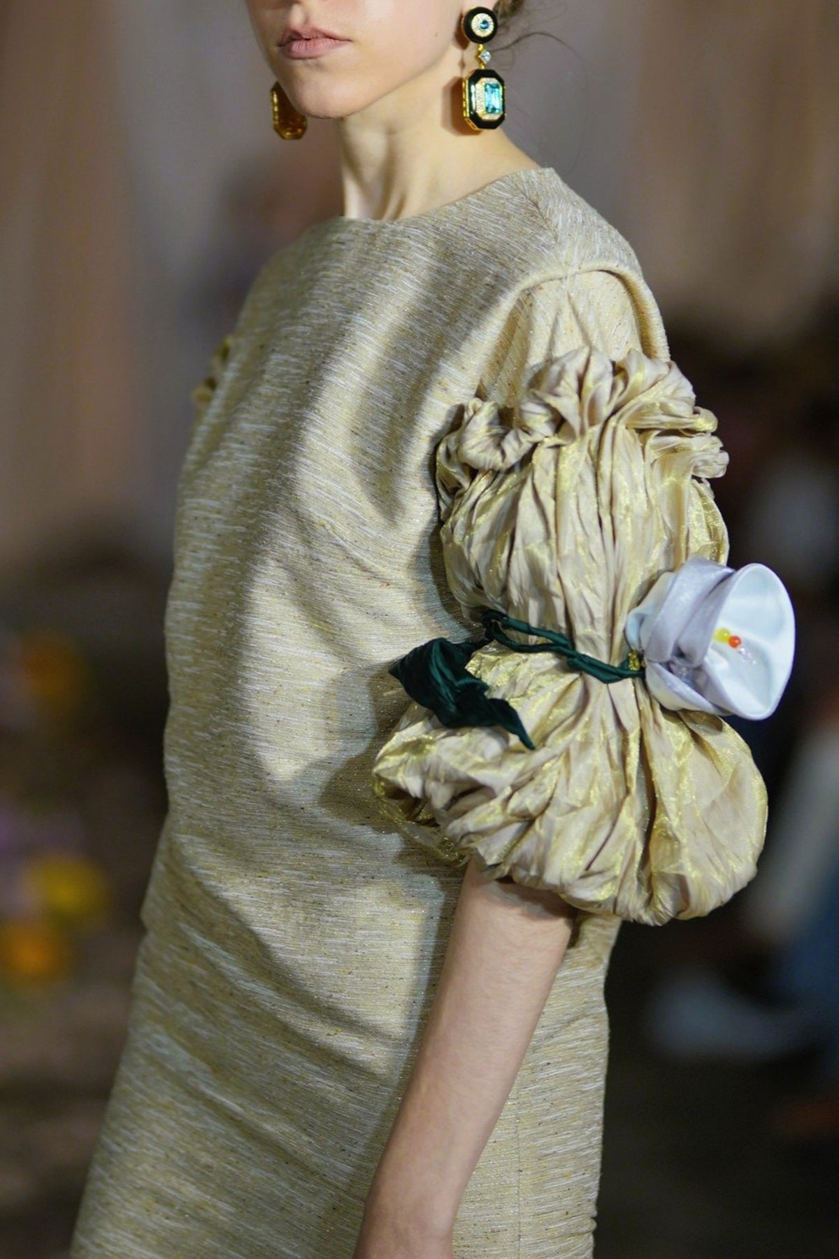 Model wearing a beige dress with a large ruffled pocket holding a white object.