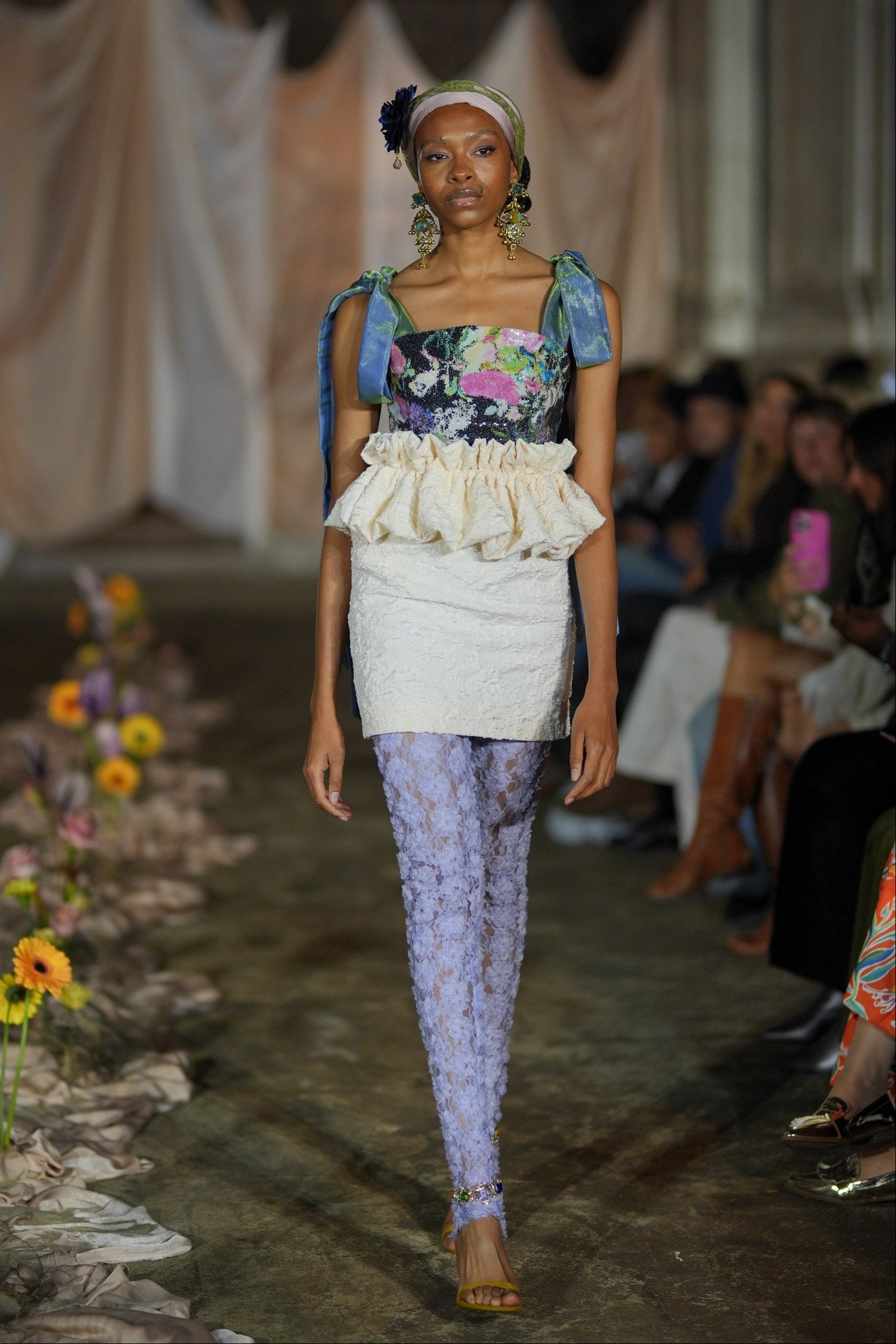 Model walking on a runway wearing a colorful outfit with floral patterns.