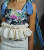 Close-up of a person wearing a floral top and textured white skirt with a blue scarf.