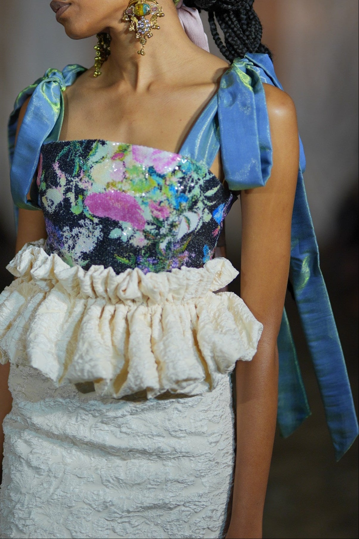 Close-up of a person wearing a floral top and textured white skirt with a blue scarf.