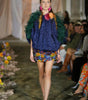 Model walking on a runway wearing a colorful outfit with floral elements.