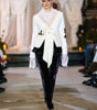 Model wearing a white cardigan and black pants on a runway.