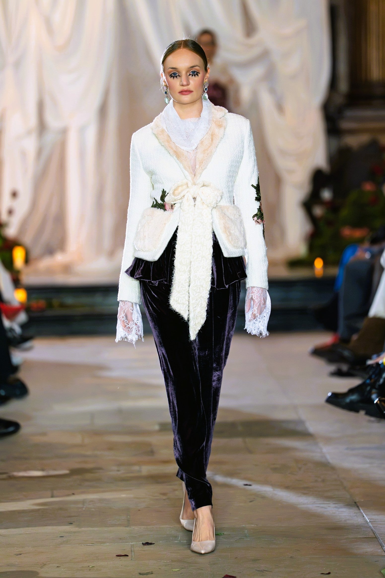 Model wearing a white cardigan and black pants on a runway.