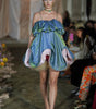 Model walking on a runway wearing a unique dress with green and blue design.