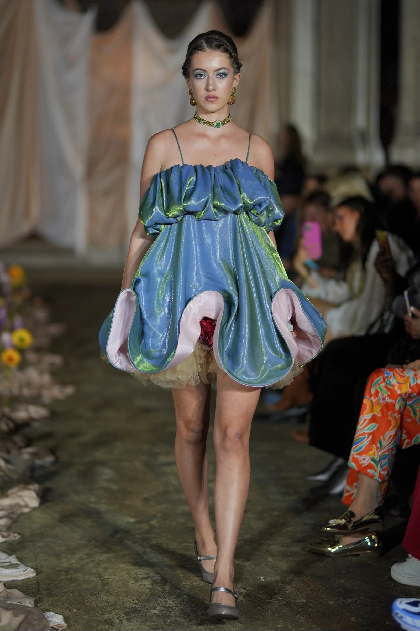 Model walking on a runway wearing a unique dress with green and blue design.