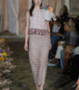 Model walking on a fashion show runway with floral decorations.