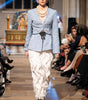 Model walking on a runway wearing a blue checkered blazer and white feathered skirt.