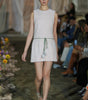 Model walking on a fashion runway wearing a light-colored dress.
