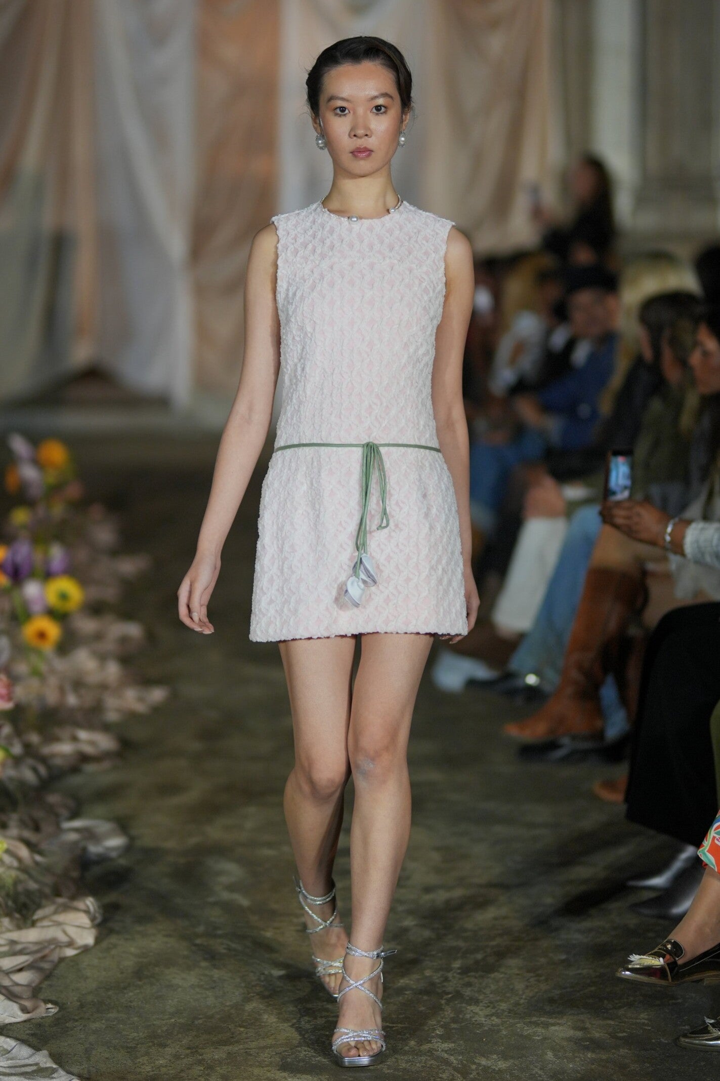 Model walking on a fashion runway wearing a light-colored dress.